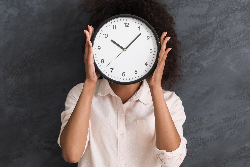 Lady holding a clock in front of her face. Time management tips for home workers.